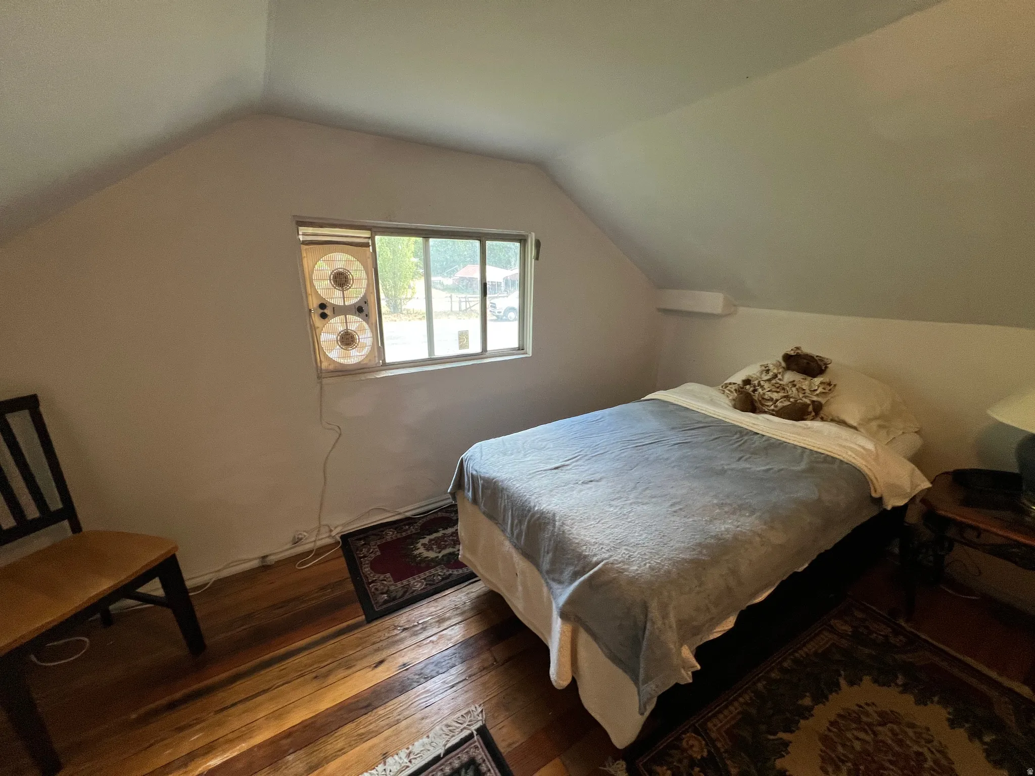 Attic room featuring sloped ceilings, a window, and wood-finish flooring