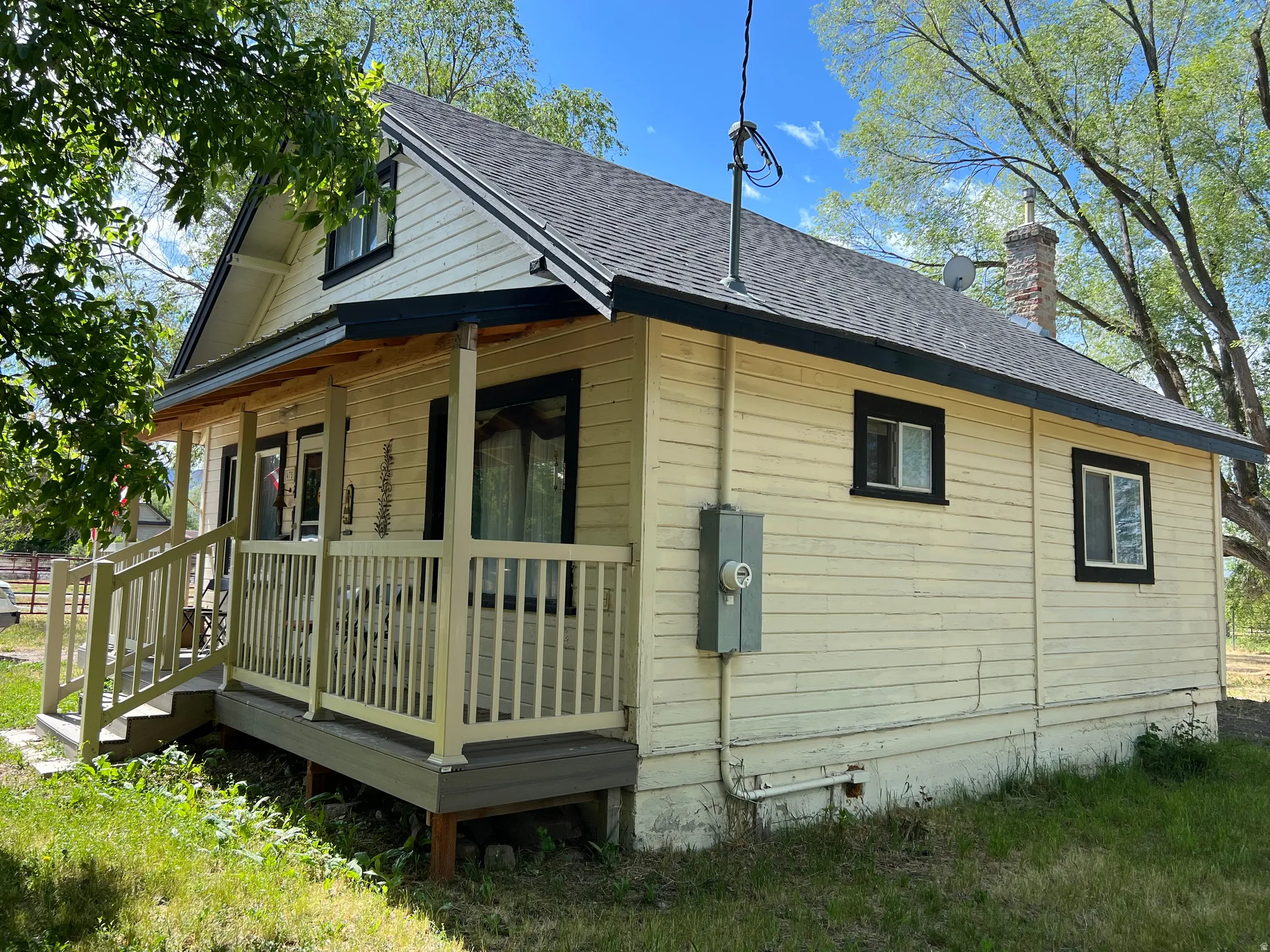 Exterior featuring a front porch with railing, light-colored siding, a dark shingle roof, dark trim windows, and a brick chimney