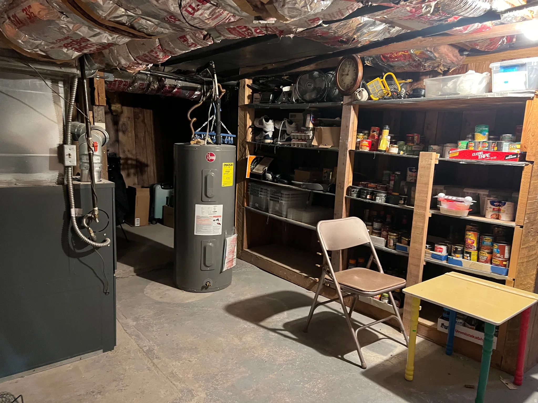 Basement utility area featuring a hot water heater, furnace, exposed ceiling insulation, and built-in shelving units