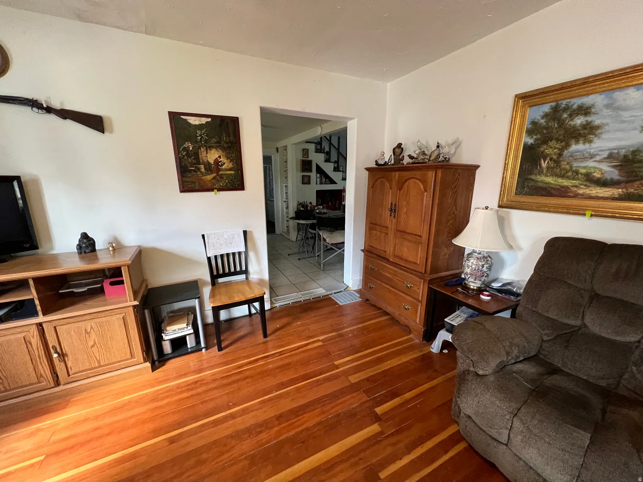 Hardwood-finish flooring, white painted walls, and a visible doorway to another area with tiled flooring