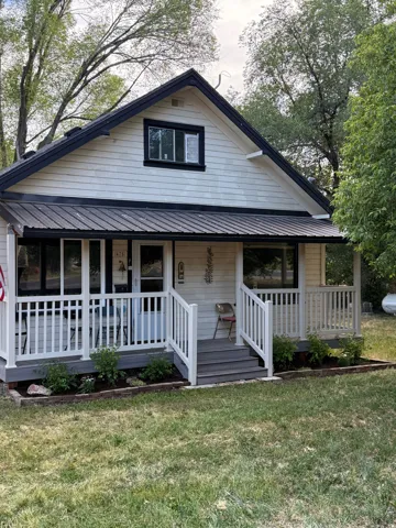 Charming single-story exterior featuring white horizontal siding, a black metal roof, and a covered front porch with white railing