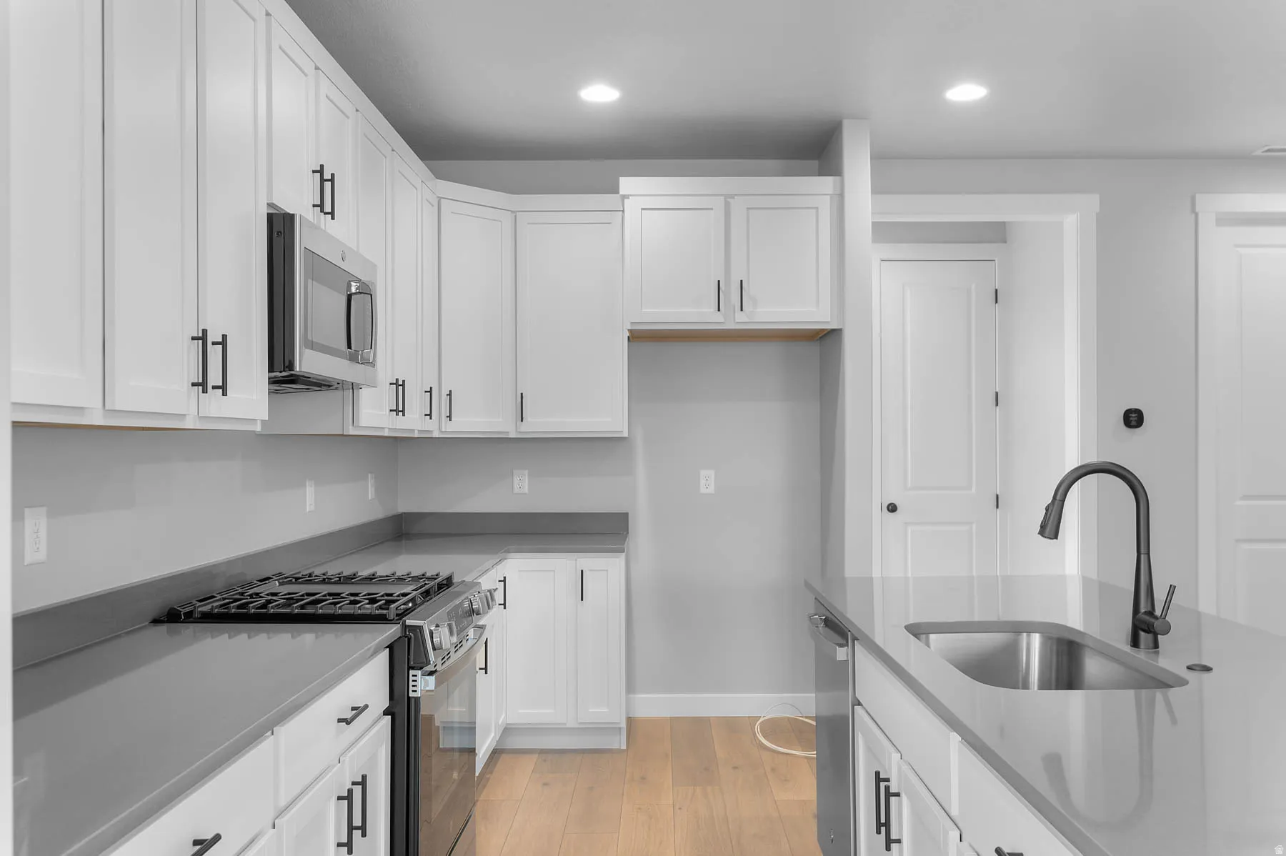 Kitchen featuring white cabinetry, dark hardware, stainless steel appliances, light wood-finish flooring, and a kitchen island with an undermount sink and matte black faucet