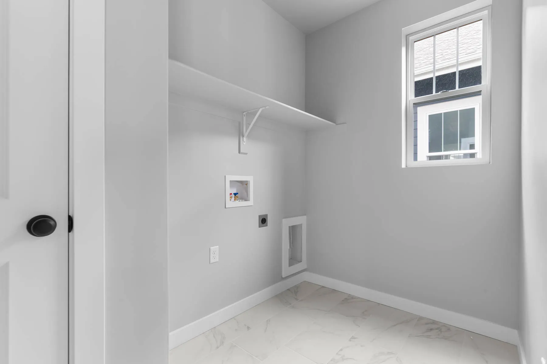 Dedicated laundry room featuring marble-look tile flooring, a built-in shelf, and a window