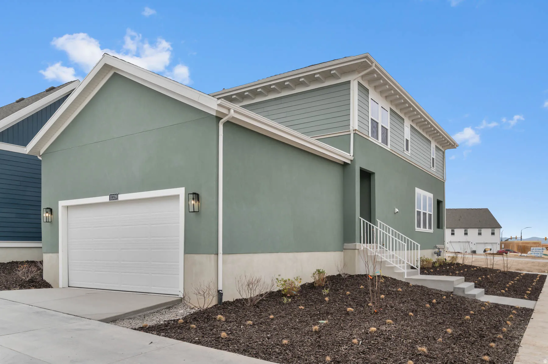 Contemporary exterior featuring stucco and horizontal siding, an integrated garage with a white door, a direct-entry door with a white railing, and exterior wall sconces