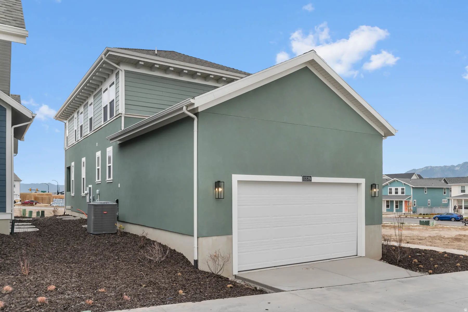 Exterior features include a two-car garage with a white overhead door, flanking wall sconces, and light green stucco siding