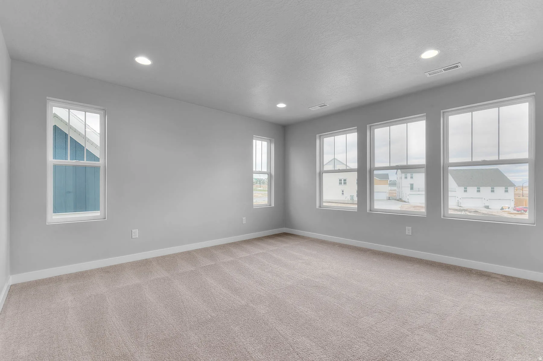 Spacious room featuring neutral carpeting, light gray walls, white trim, recessed lighting, and multiple windows providing ambient illumination