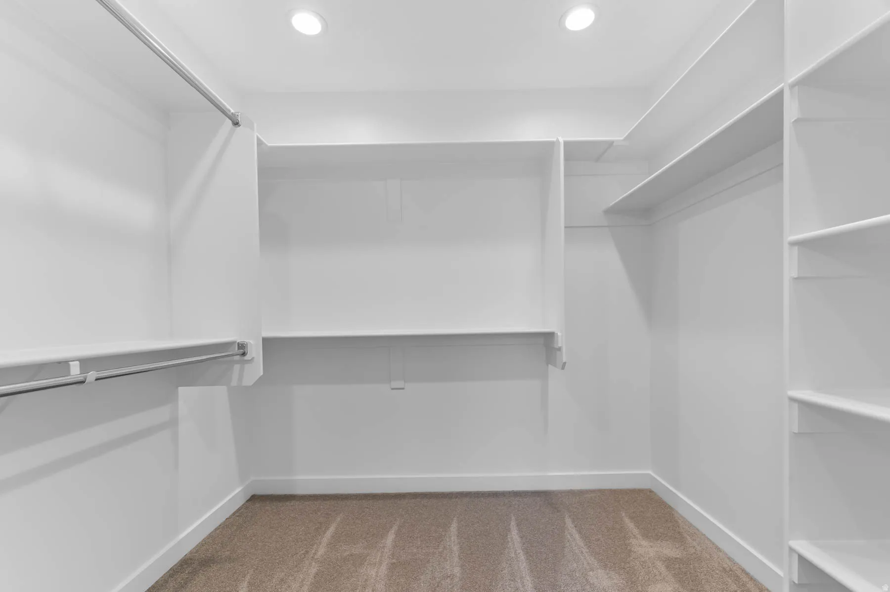 Walk-in closet featuring built-in white shelving, hanging rods, recessed lighting, and carpet flooring