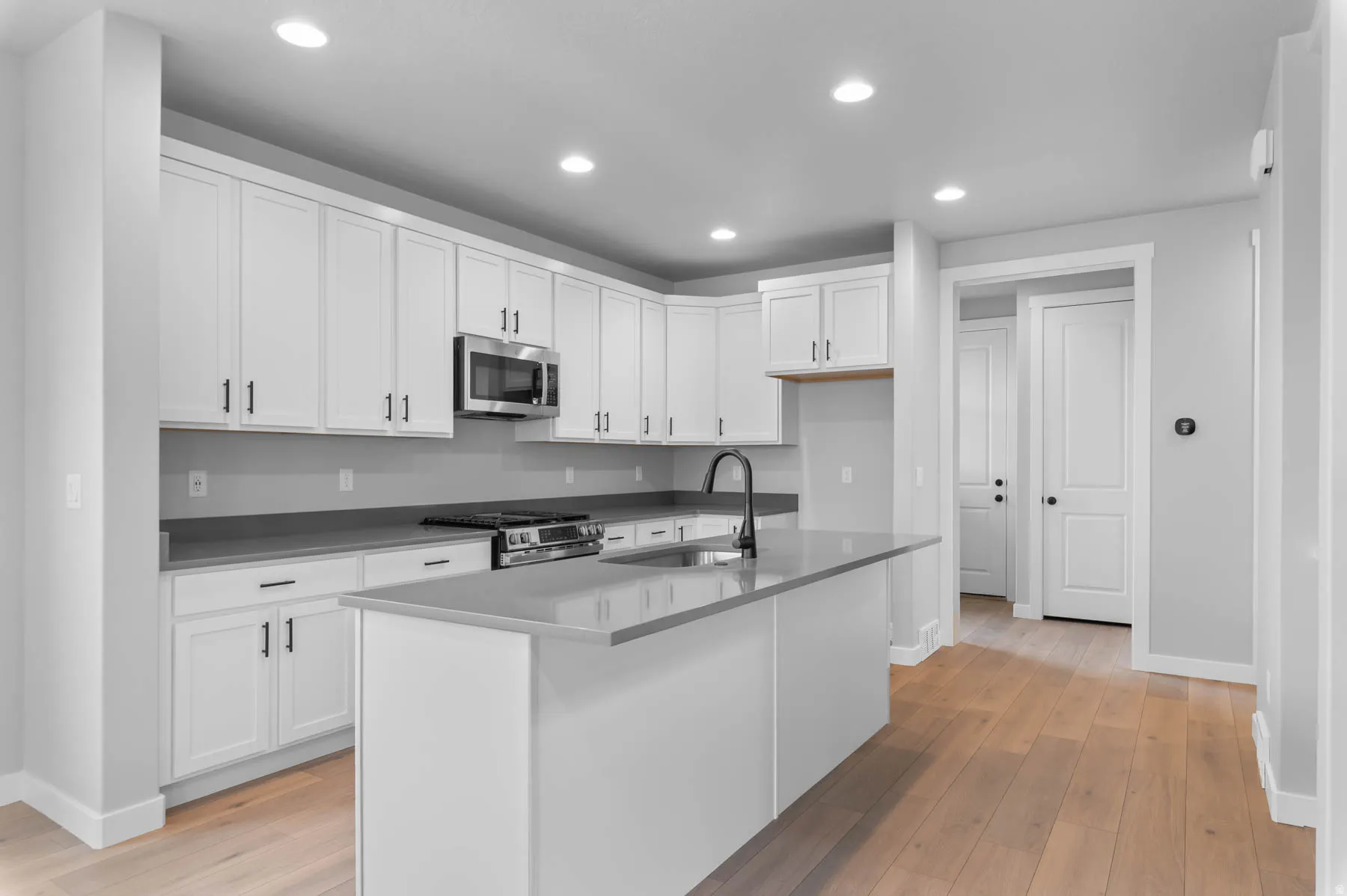 Modern kitchen featuring an expansive center island, white shaker cabinetry with dark hardware, stainless steel microwave, gas range, and wood-finish flooring