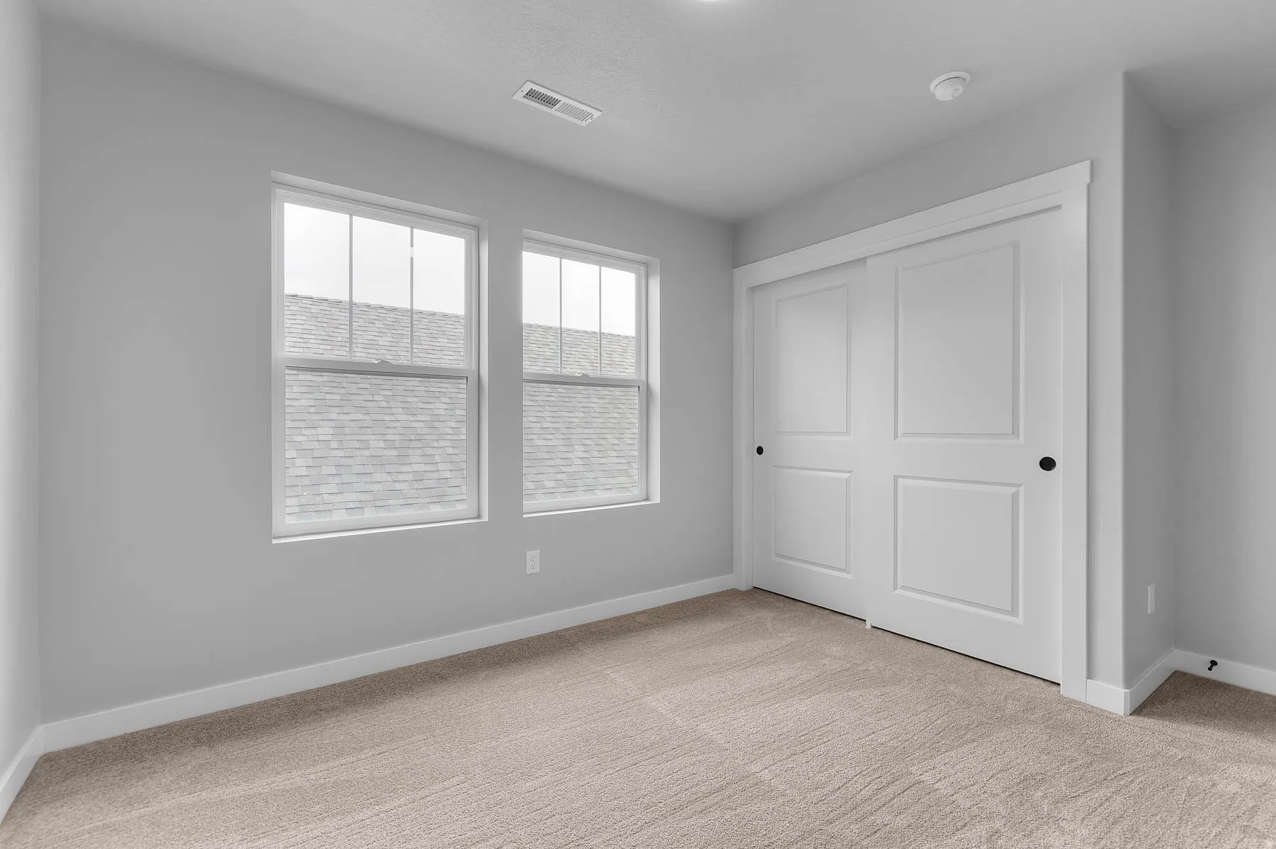 Carpeted room featuring two large windows, painted walls, white baseboards, and a bi-fold closet with panel doors and black hardware