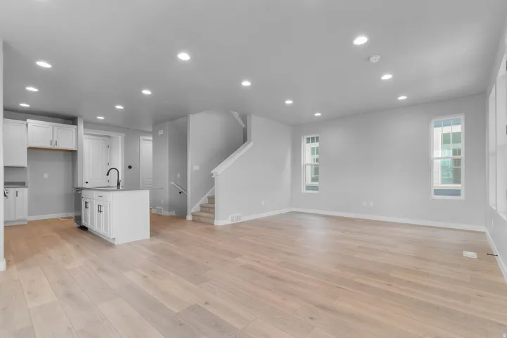 Open-concept living space featuring light wood-finish flooring, recessed lighting, white shaker cabinetry, an island with a black faucet, and multiple windows with white trim