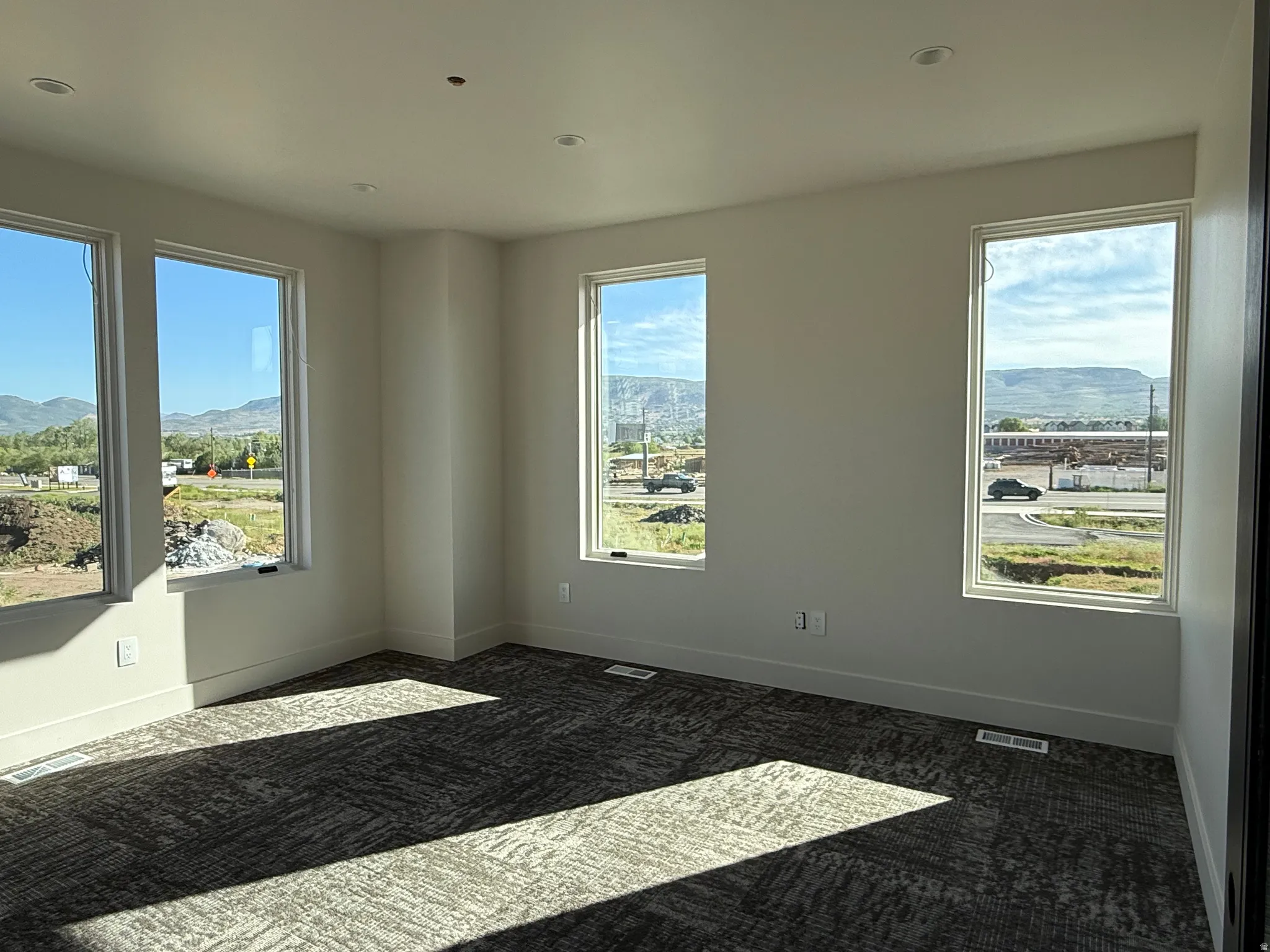 Spacious room featuring multiple large windows, recessed ceiling lighting, and patterned carpet flooring