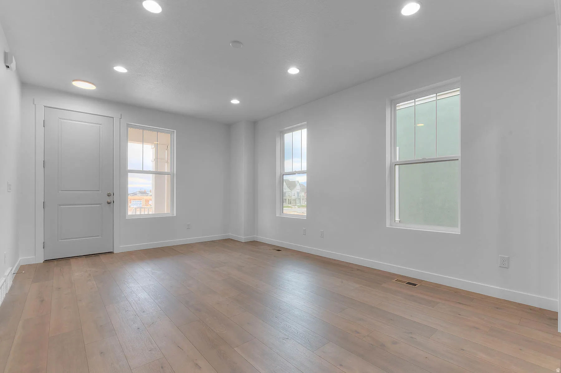 Spacious room featuring light wood-finish flooring, recessed ceiling lighting, and multiple windows with white trim