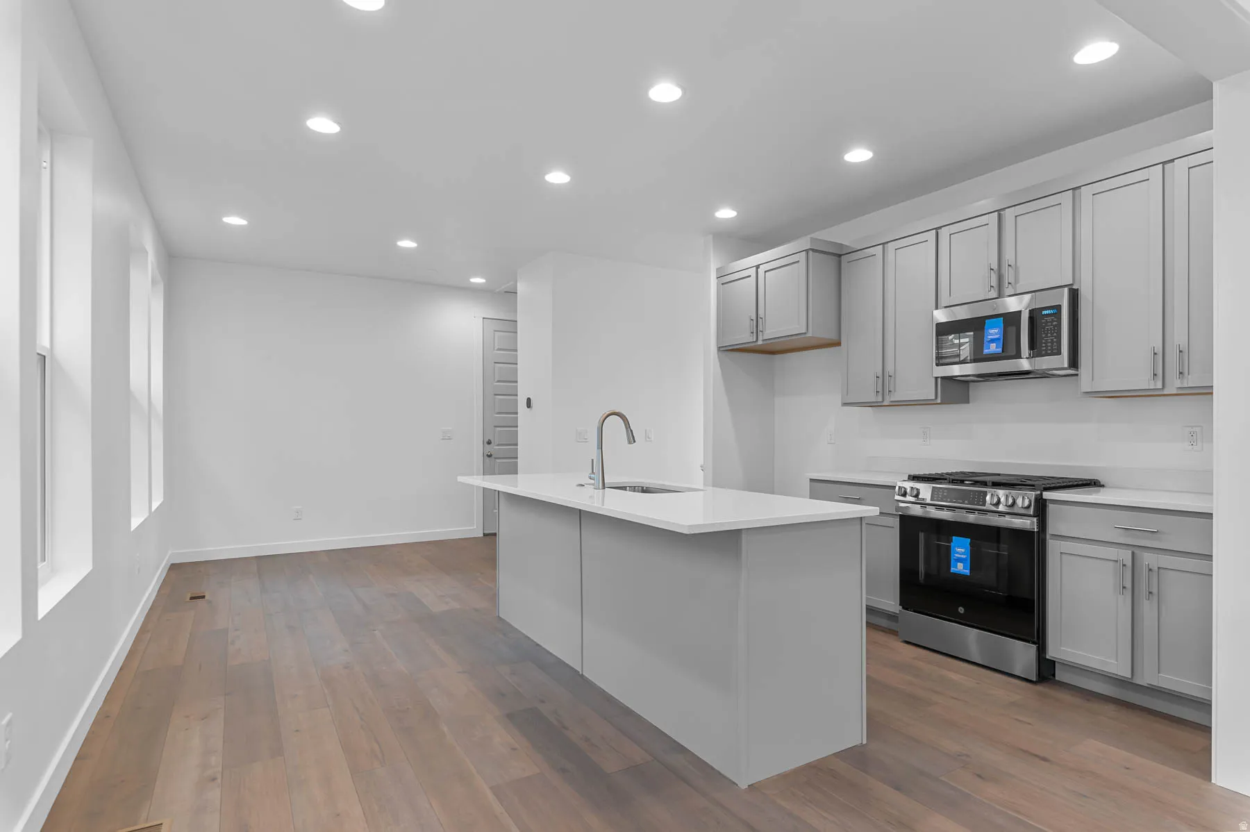 Modern kitchen featuring light gray cabinetry, stainless steel appliances, a white subway tile backsplash, and a central island with an integrated sink and gooseneck faucet