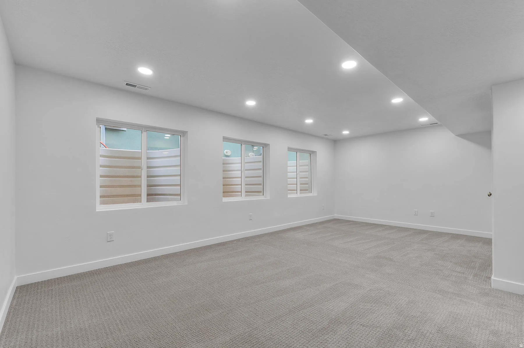 Spacious room with light gray carpeting, recessed ceiling lighting, three egress windows, and painted white walls