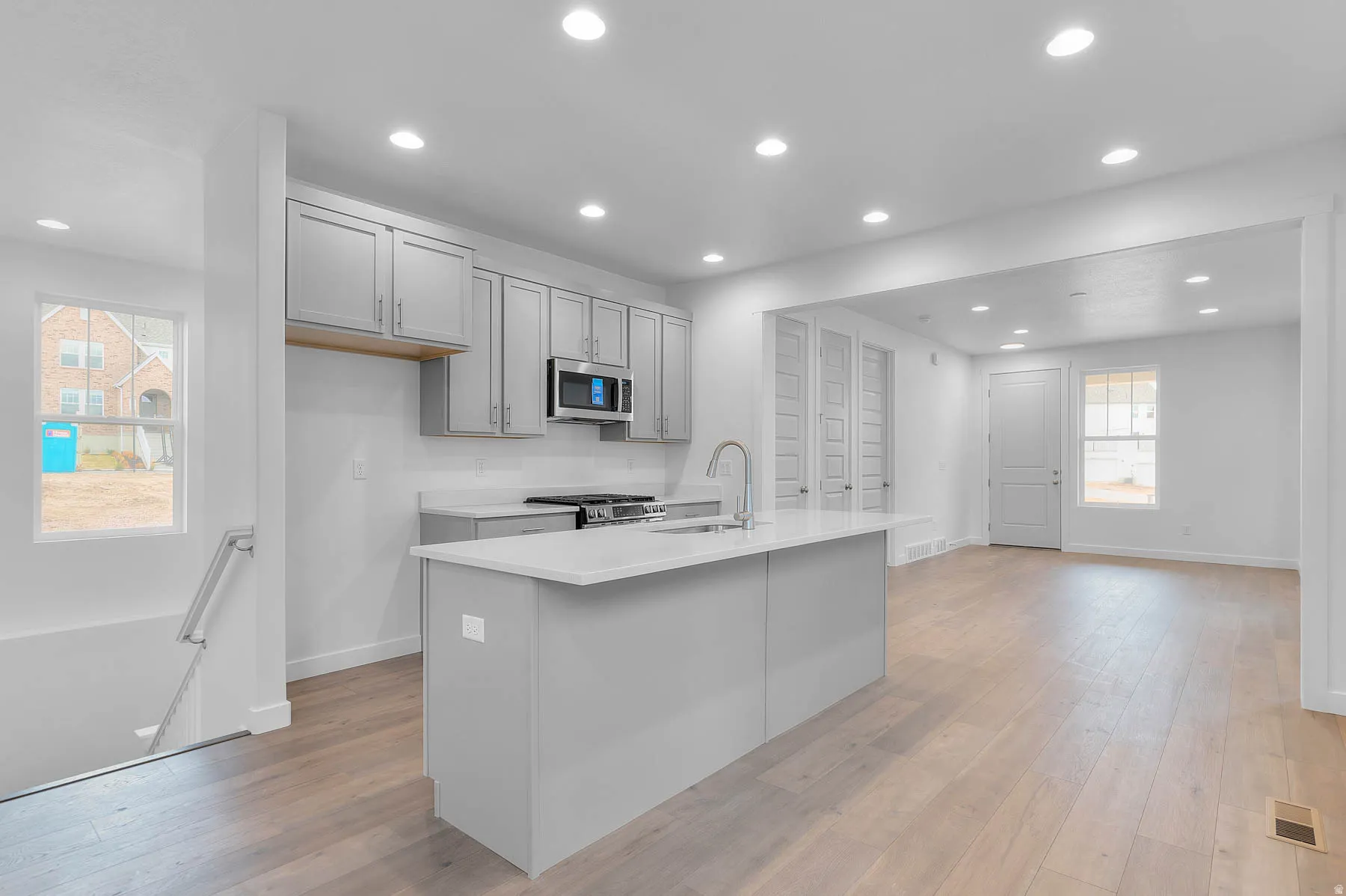 Bright kitchen featuring light gray cabinetry, a central island with countertop seating, stainless steel appliances, and wood-finish flooring
