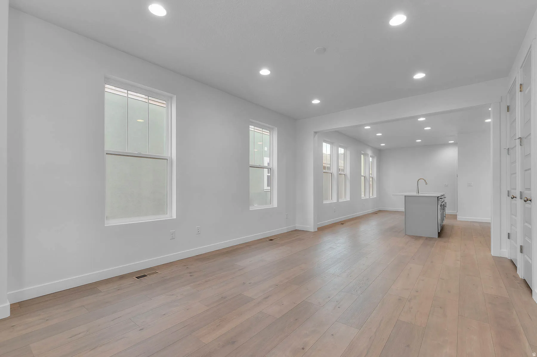 Open-concept living area featuring light wood-finish flooring, recessed lighting, and multiple windows