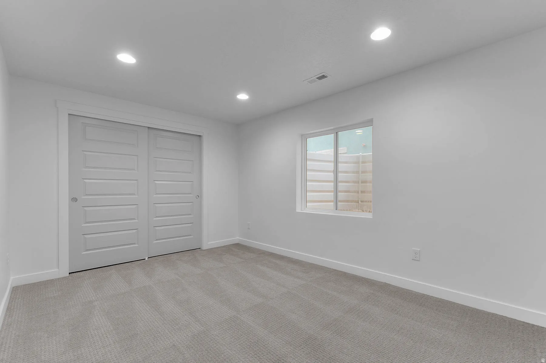 Carpeted room featuring a window with a window well, recessed lighting, and white bi-fold closet doors