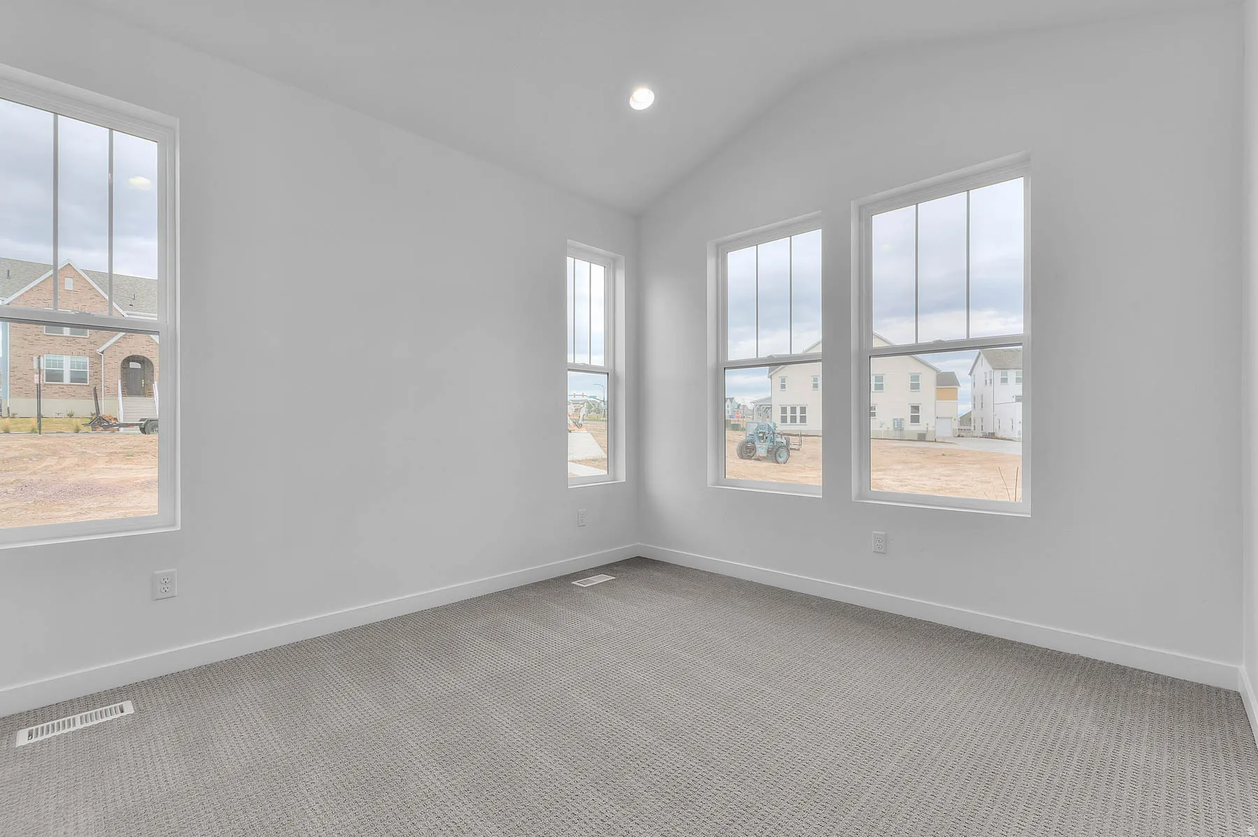 Spacious room featuring vaulted ceilings, a single recessed light fixture, four large windows, white baseboards, and neutral-toned carpet flooring