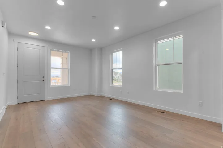 Spacious room featuring light wood-finish flooring, recessed ceiling lighting, and multiple windows with white trim
