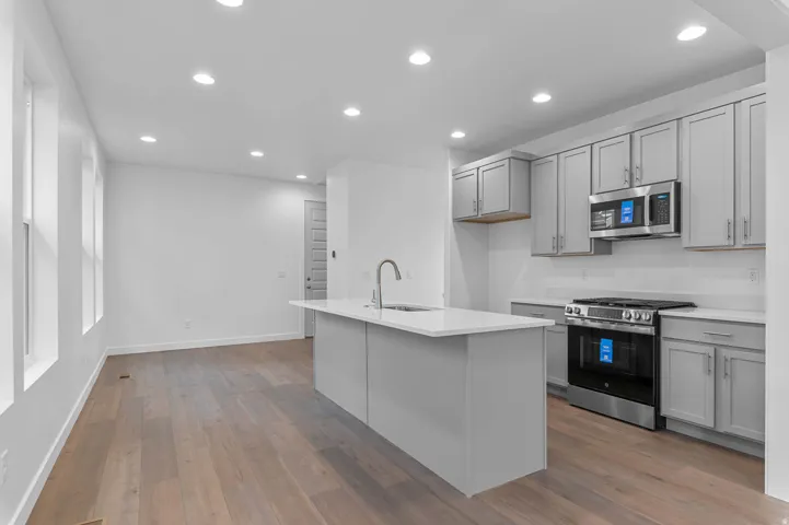 Modern kitchen featuring light gray cabinetry, stainless steel appliances, a white subway tile backsplash, and a central island with an integrated sink and gooseneck faucet