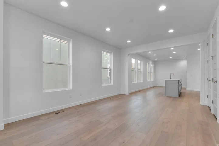 Open-concept living area featuring light wood-finish flooring, recessed lighting, and multiple windows