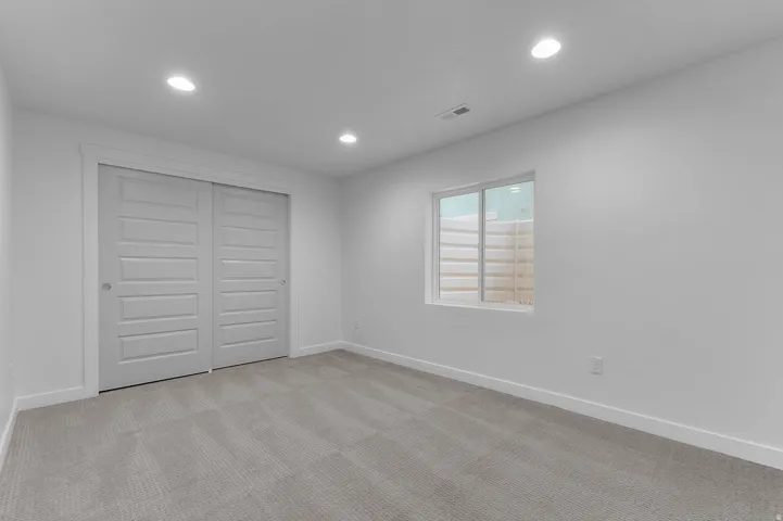 Carpeted room featuring a window with a window well, recessed lighting, and white bi-fold closet doors