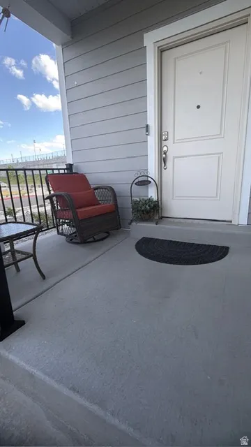 Inviting concrete front porch with gray siding and a white entry door featuring a door knocker and deadbolt