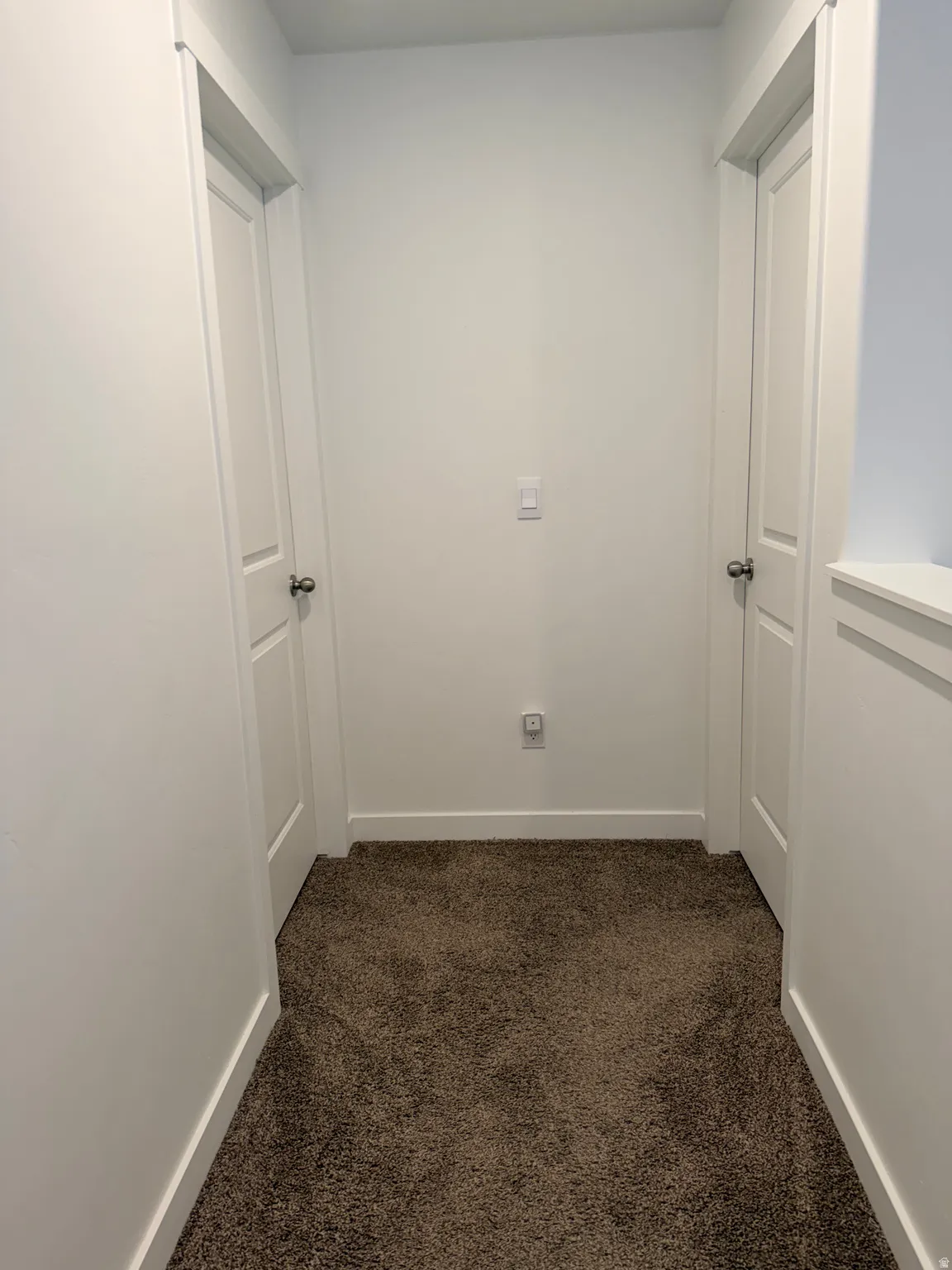 Hallway with plush brown carpeting, white walls, and white trim
