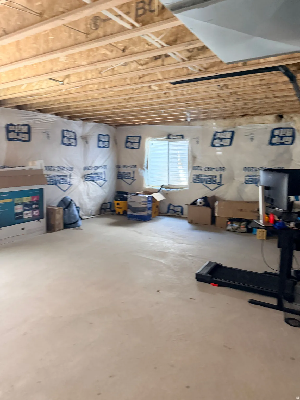 Unfinished basement space featuring visible floor joists, concrete flooring, and insulated perimeter walls