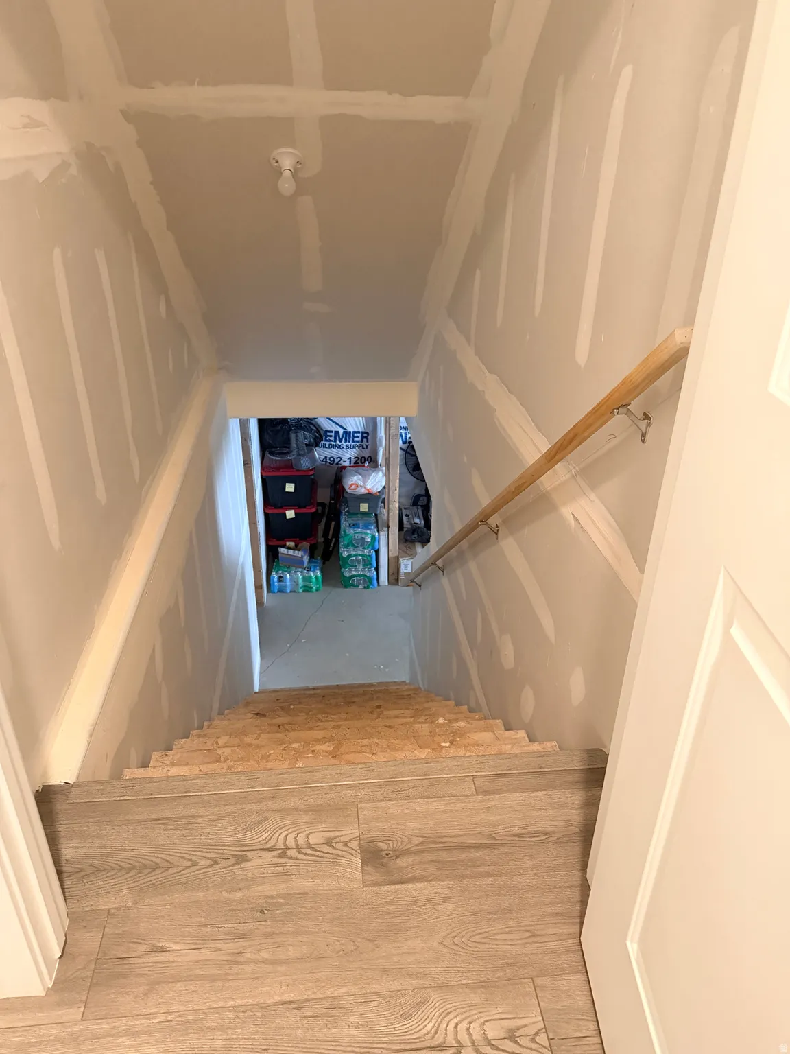 Stairwell featuring wood-finish plank flooring, bare wood stair treads, an unpainted sheetrock wall finish, and a wood handrail