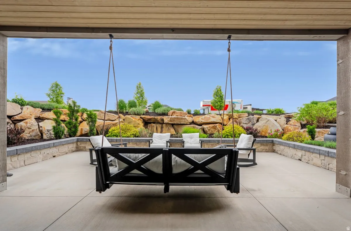 Covered outdoor patio with concrete flooring, stone retention walls, and tiered landscaping