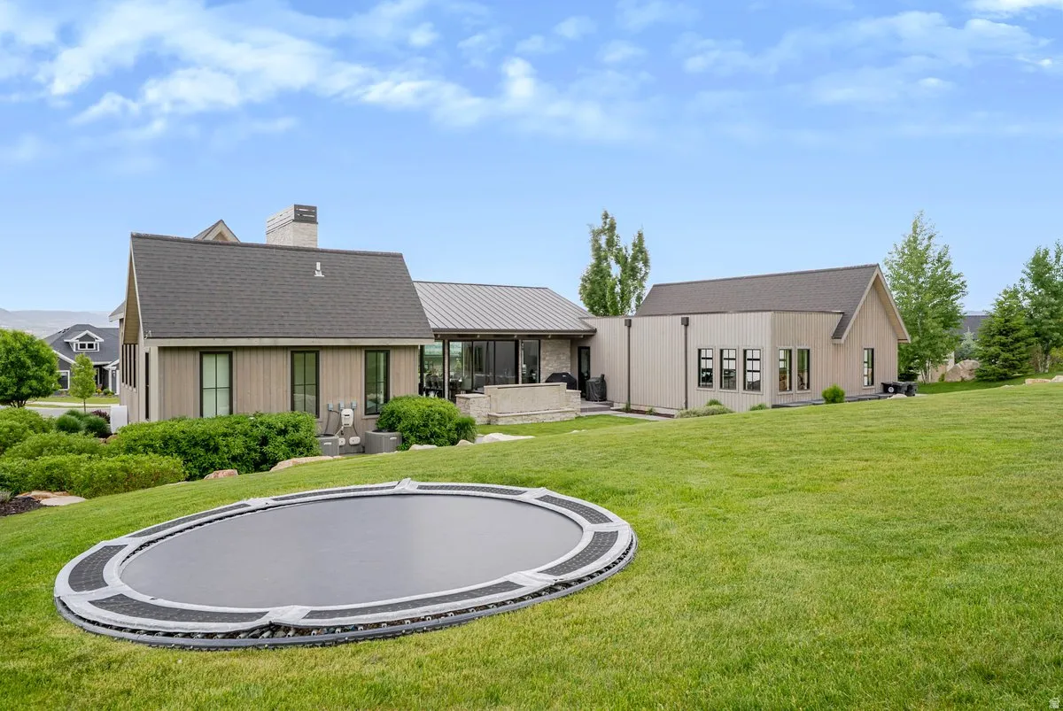 Expansive green lawn with a built-in trampoline, complemented by a contemporary exterior design featuring vertical siding and dark-trimmed windows