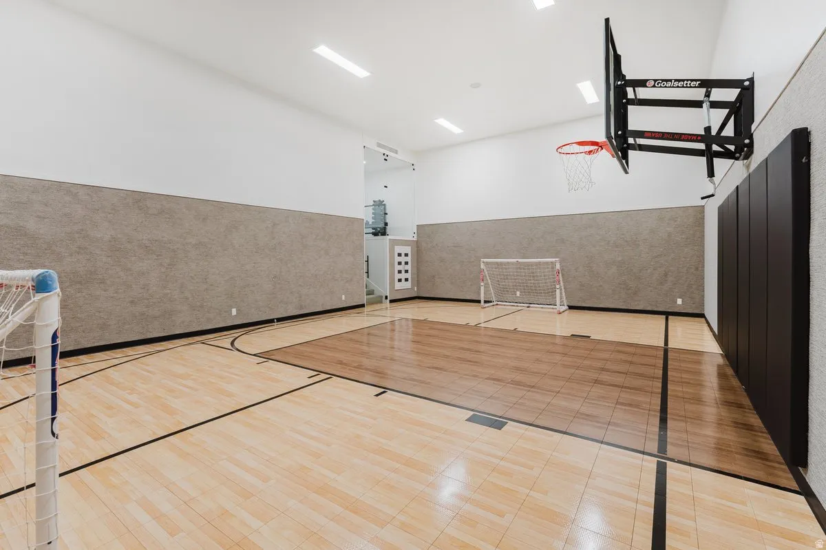 Indoor athletic court featuring hardwood flooring with court markings, an adjustable basketball hoop, and padded wall protection
