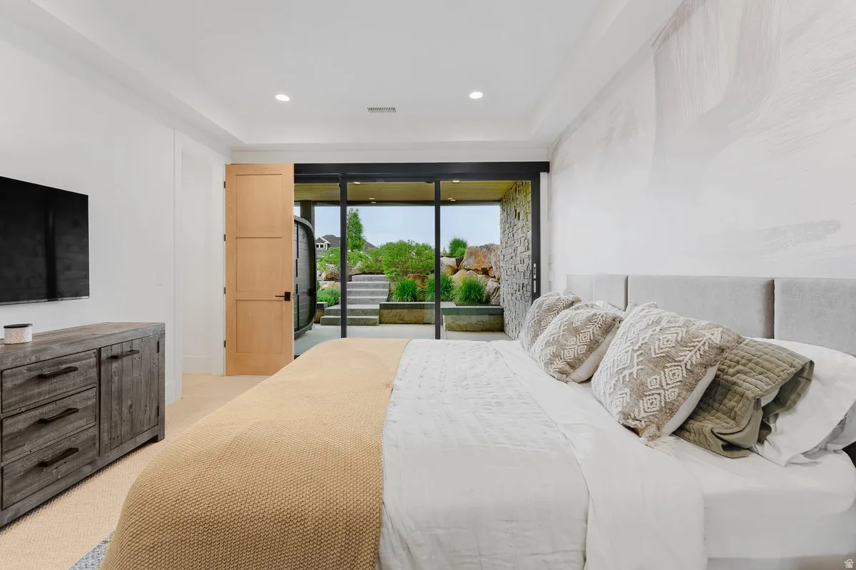 Recessed lighting illuminating a spacious room with a light wood-finish door and a large glass sliding door opening to an outdoor patio with stone steps and landscaping