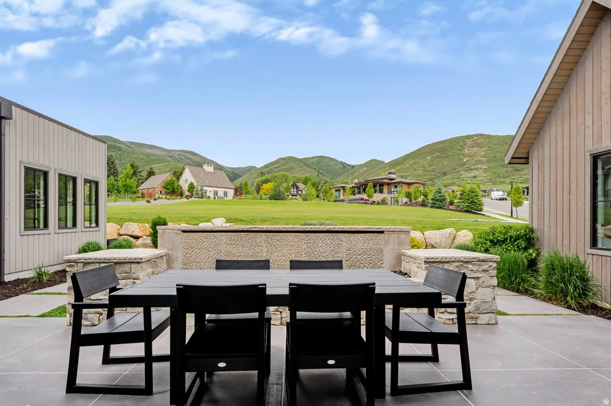Expansive patio featuring large format concrete pavers, a textured stone privacy wall, and built-in stone planters, all set against a backdrop of rolling green hills