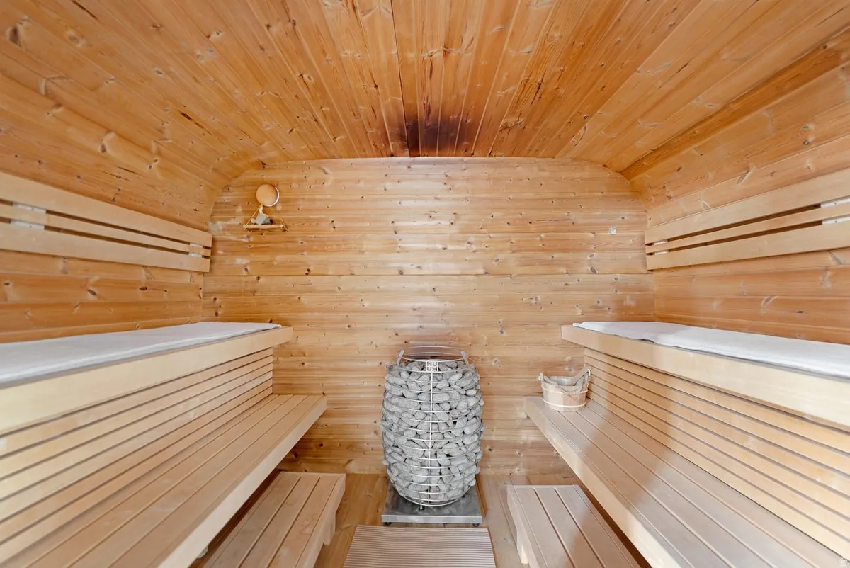 Interior sauna featuring tongue-and-groove wood paneling, multi-tiered wood benches, and a central rock heater