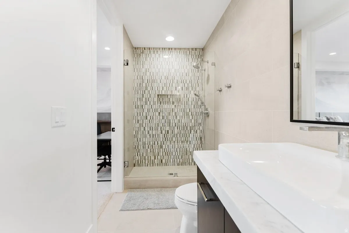 Contemporary bathroom featuring a glass-enclosed shower with mosaic tile, a sleek rectangular vessel sink, and a floating vanity with a light-colored countertop