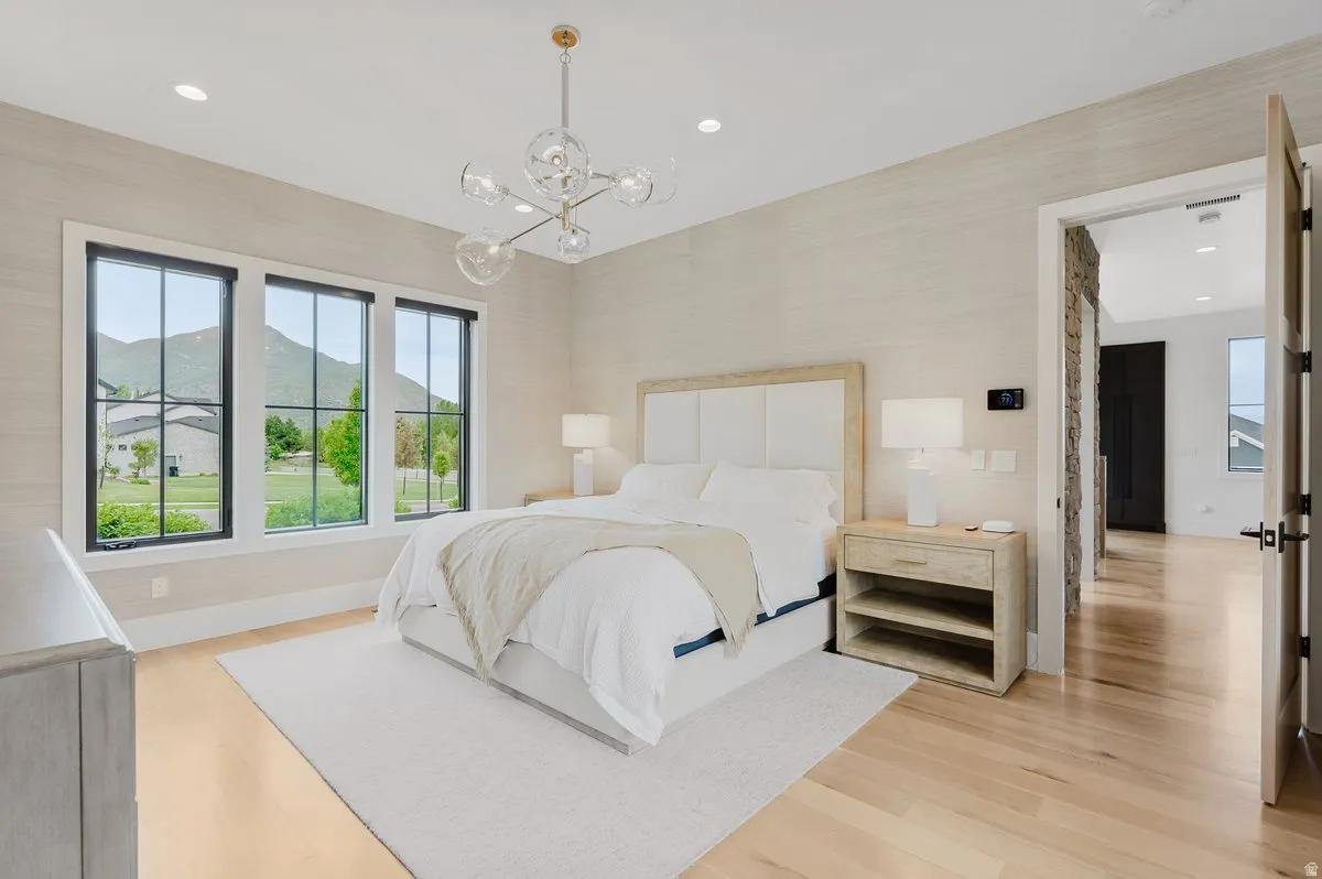 Bedroom featuring multiple black-framed windows, hardwood flooring, and a modern chandelier