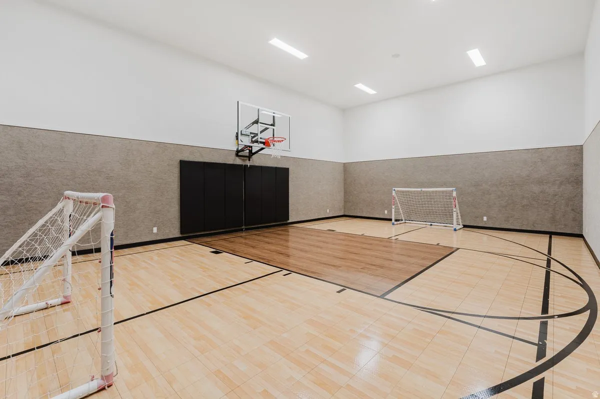 Indoor sport court featuring light wood-finish flooring with court markings, a basketball hoop, and padded wall sections
