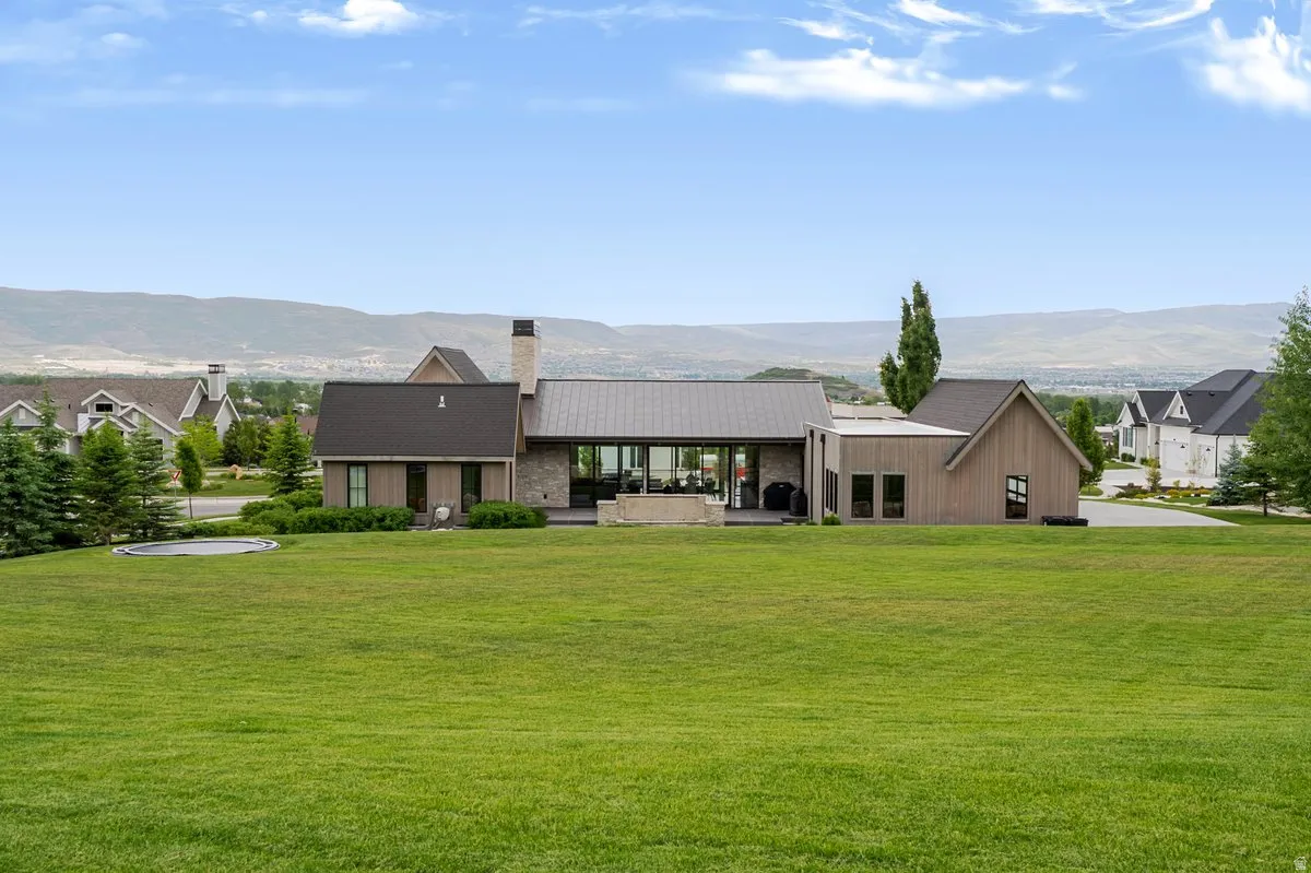 Expansive rear exterior featuring a stone and wood-paneled facade, a covered patio, a large green lawn, and distant mountains