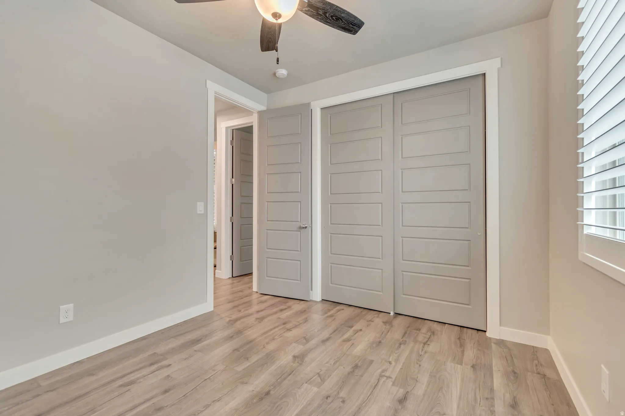 Neutral tone walls with white trim, wood-finish flooring, a ceiling fan with integrated lighting, and a window with horizontal blinds