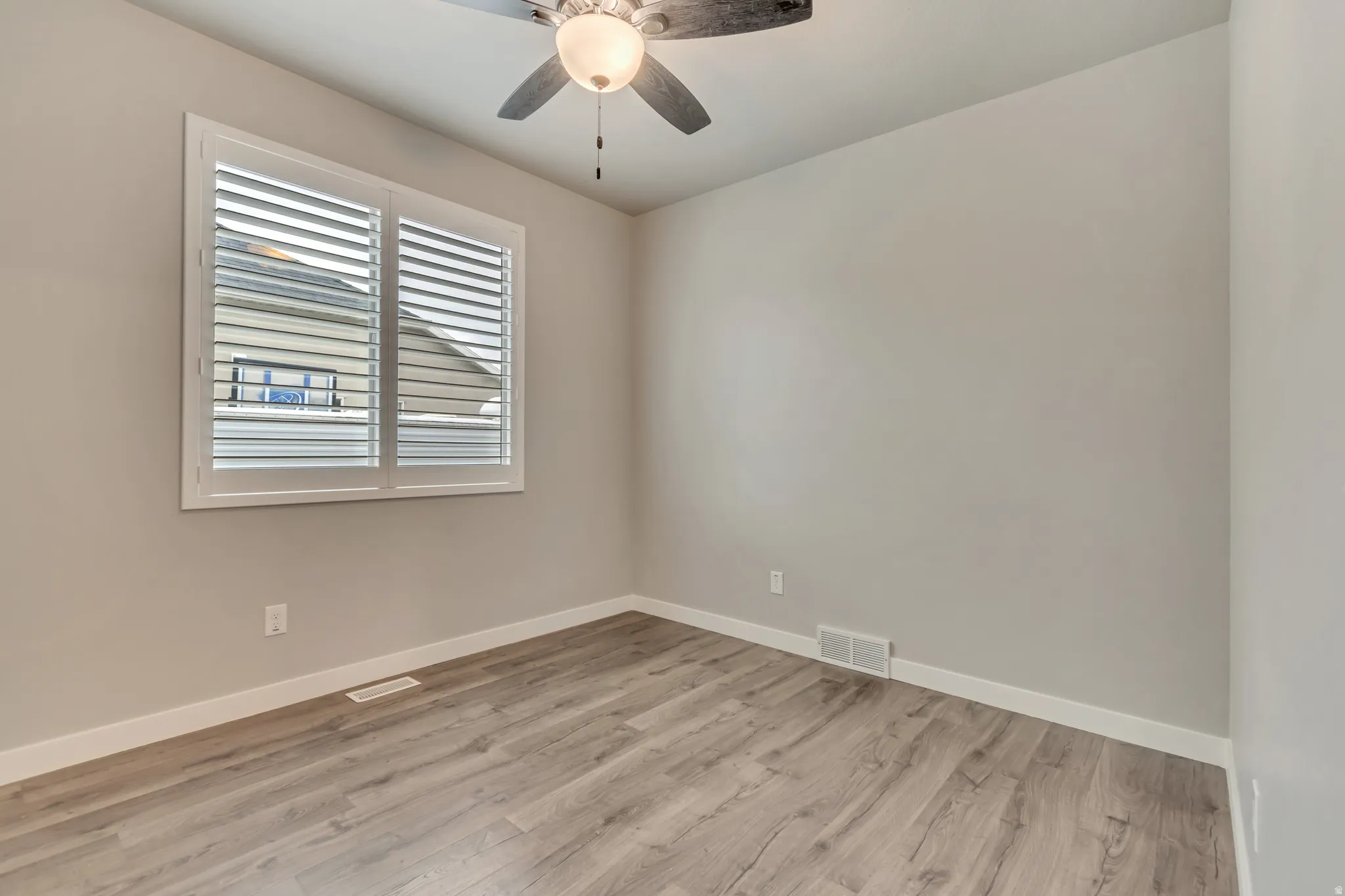 Interiors featuring wood-finish flooring, light gray walls, white trim, and a window with plantation shutters