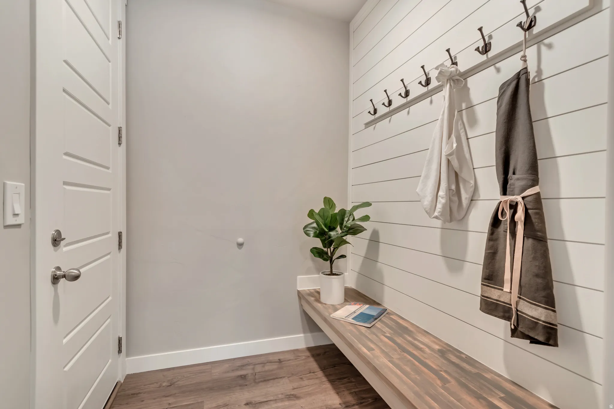 Entryway mudroom featuring a built-in wood bench, shiplap accent wall, and wood-finish flooring