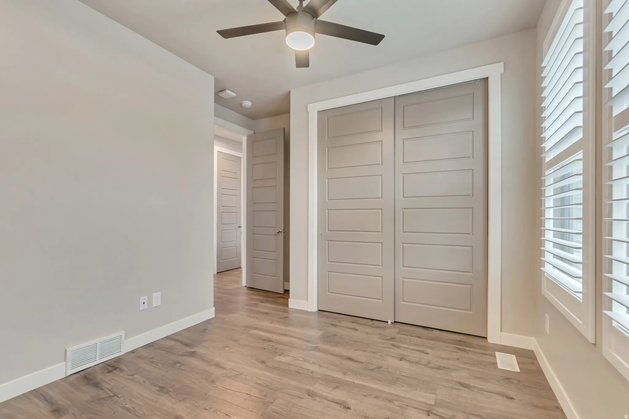 Room featuring wood-finish flooring, plantation shutters, a contemporary ceiling fan, and a built-in closet with paneled doors