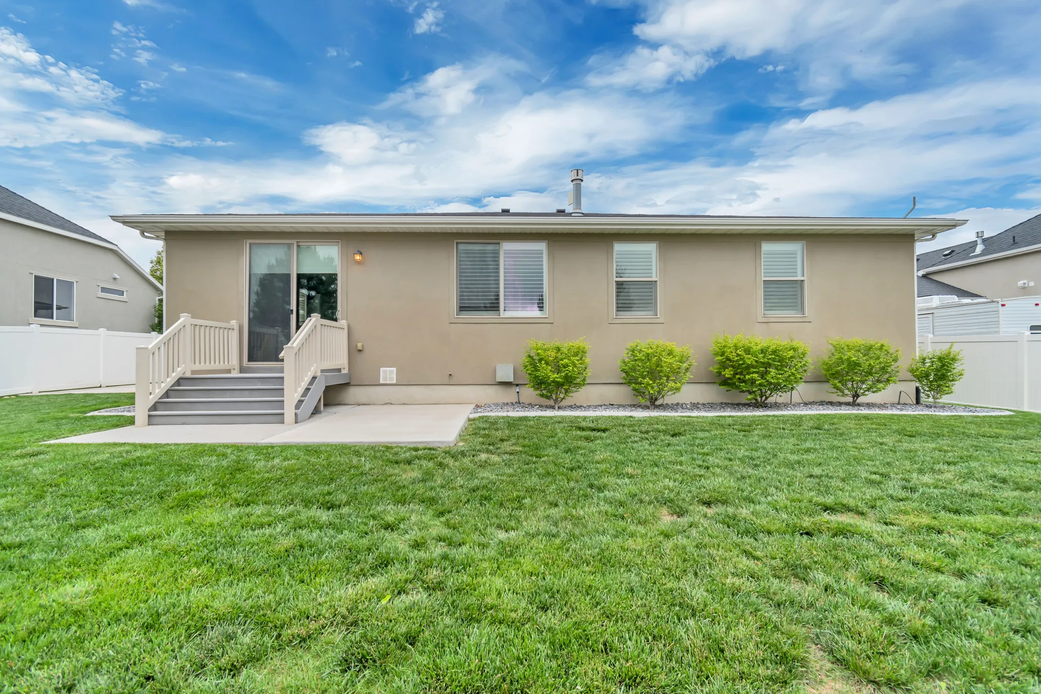 Expansive green lawn with a concrete patio and steps leading to a sliding glass door