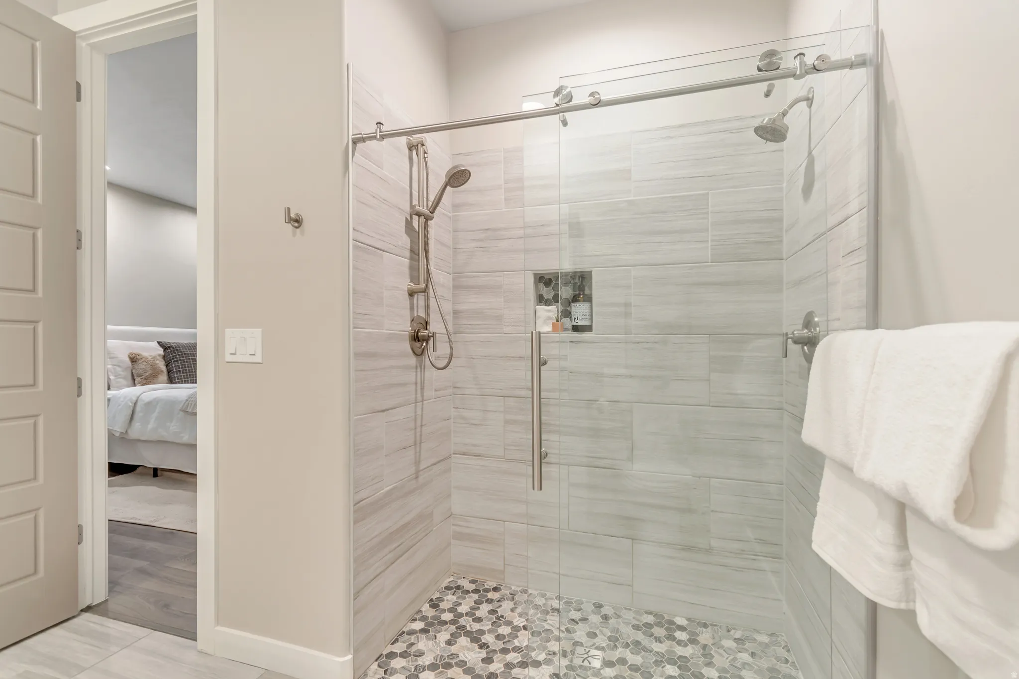 Spacious walk-in shower featuring a glass enclosure with a sliding door, dual shower heads, integrated wall niche, and a mosaic tile floor