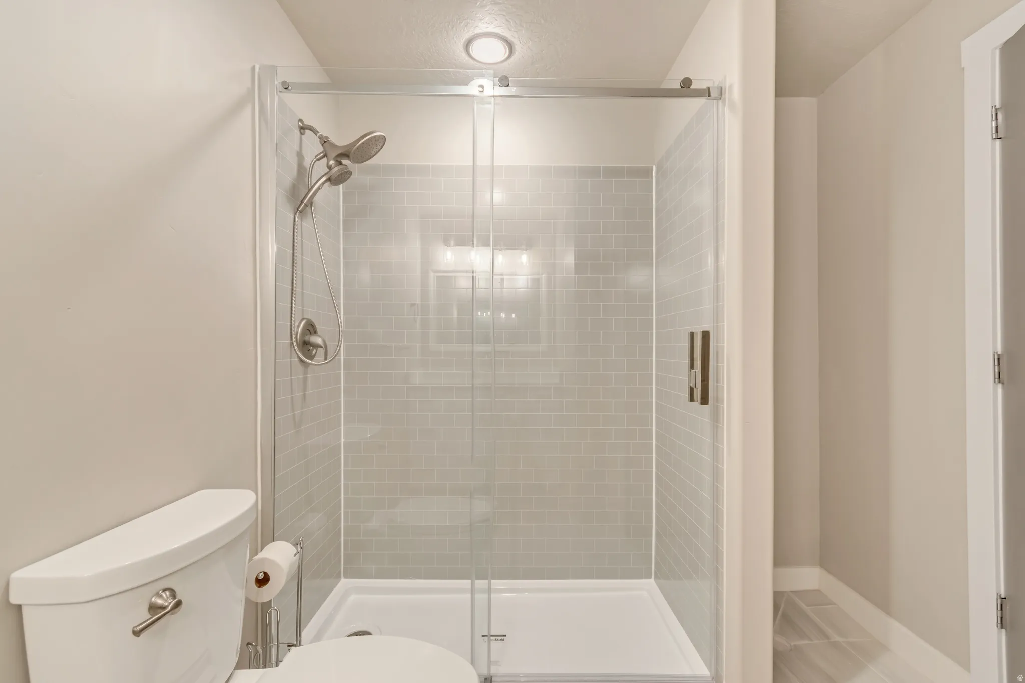Glass-enclosed shower with light gray subway tile surround and brushed nickel fixtures