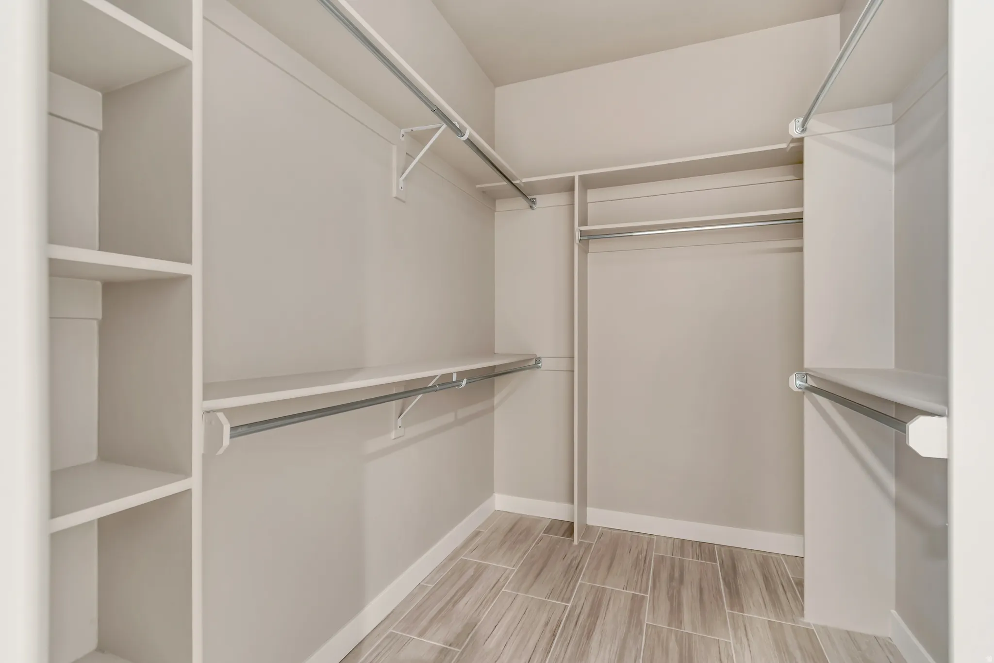 Walk-in closet featuring extensive built-in shelving, multiple hanging rods, and wood-look tile flooring