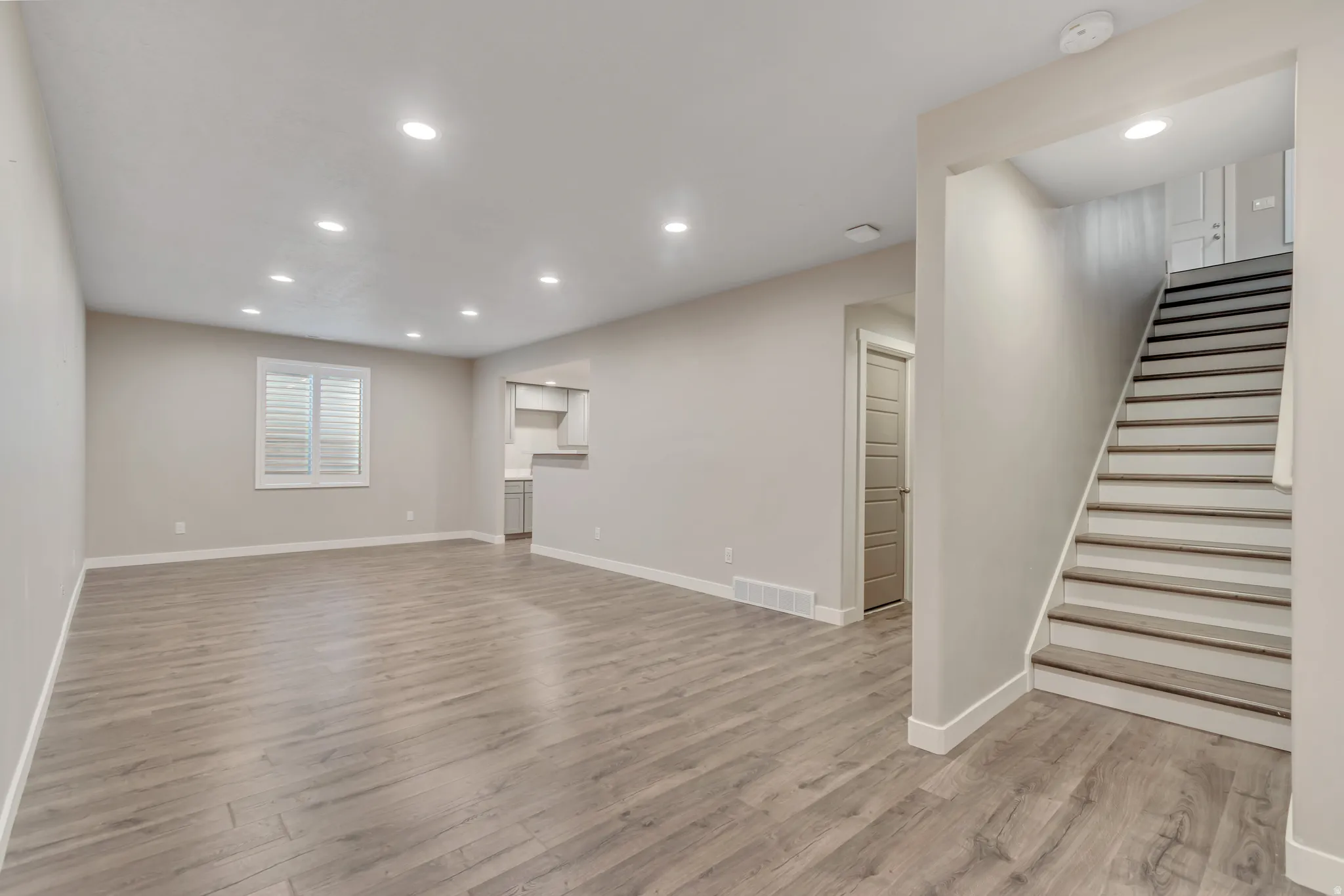 Spacious living area featuring wood-finish flooring, recessed lighting, and a white plantation-shutter window