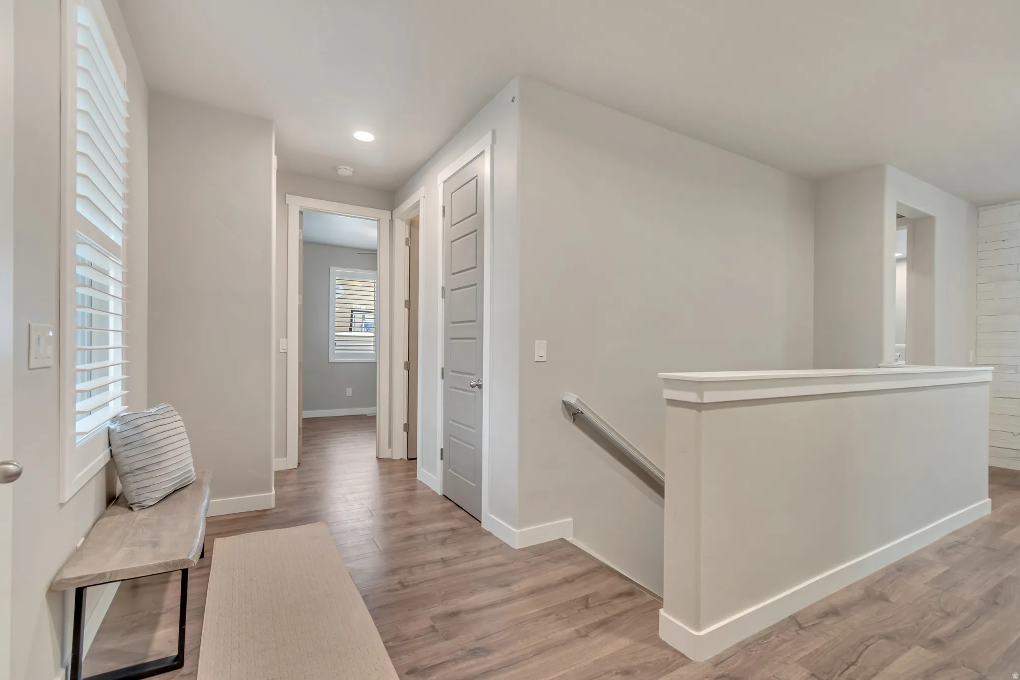 Spacious hallway featuring wood-finish flooring, recessed lighting, plantation shutters, and light gray interior doors